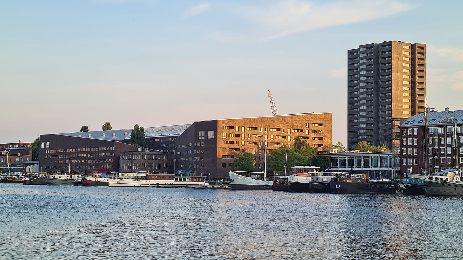 Modernos edificios residenciales y barcos amarrados bordean el paseo marítimo de Java Island y KNSM Island en Ámsterdam al atardecer.