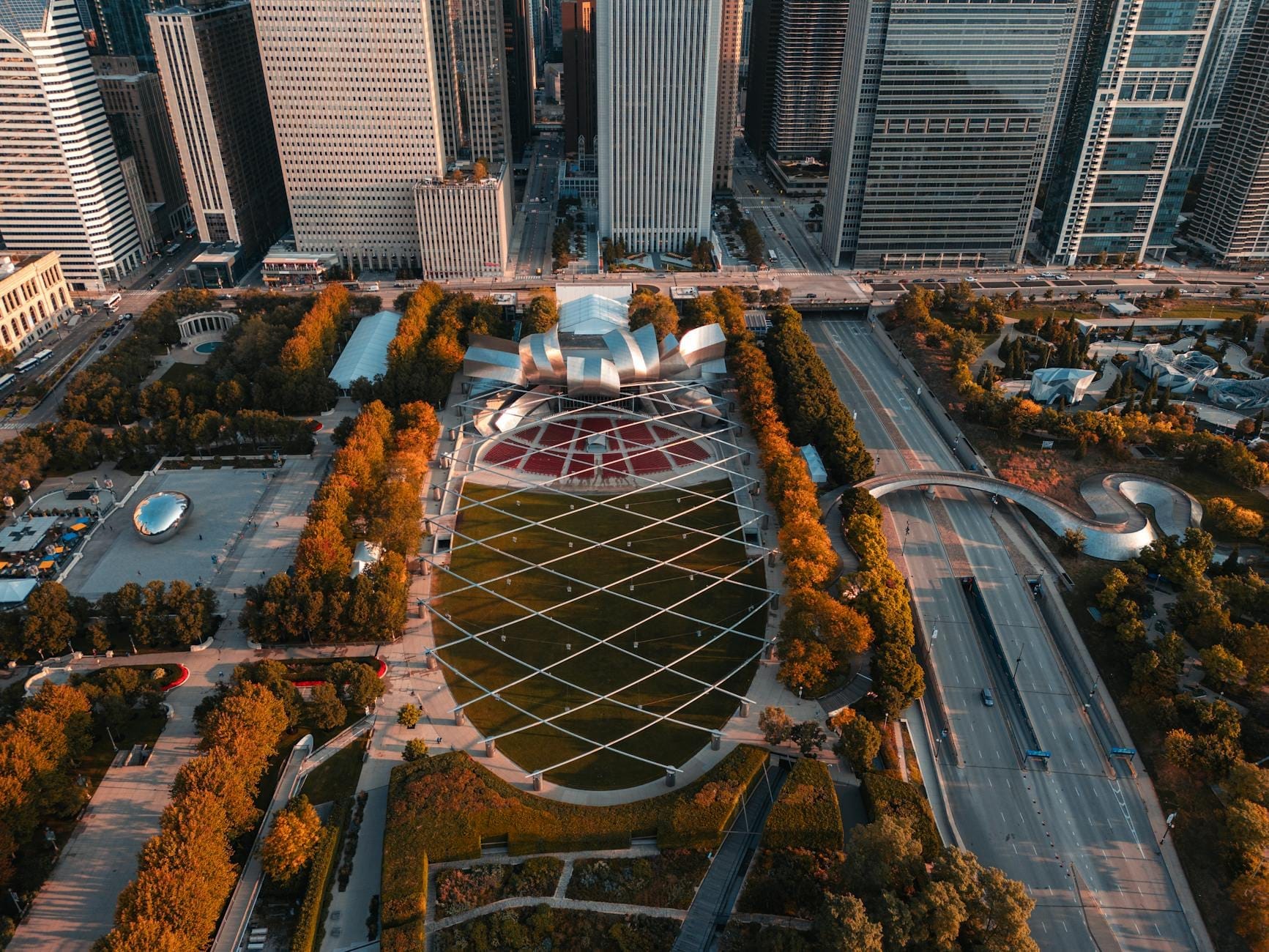 Vista aerea del Jay Pritzker Pavilion con la sua caratteristica struttura metallica, il grande prato e i grattacieli del centro di Chicago in una giornata luminosa.