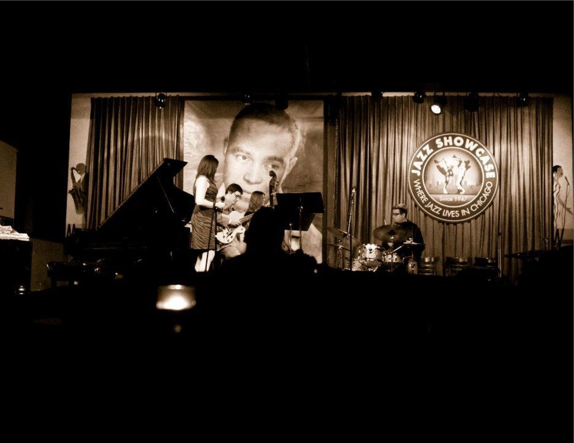 Una band jazz dal vivo si esibisce sul palco fiocamente illuminato del Jazz Showcase a Chicago, con musicisti al pianoforte, alla chitarra e alla batteria.