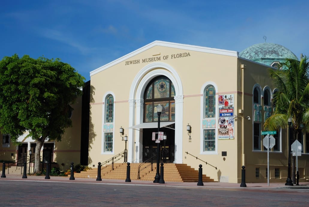 Vista frontale del Jewish Museum of Florida–FIU, con la sua facciata gialla, le vetrate colorate e la prominente cupola in rame sotto un cielo azzurro limpido.