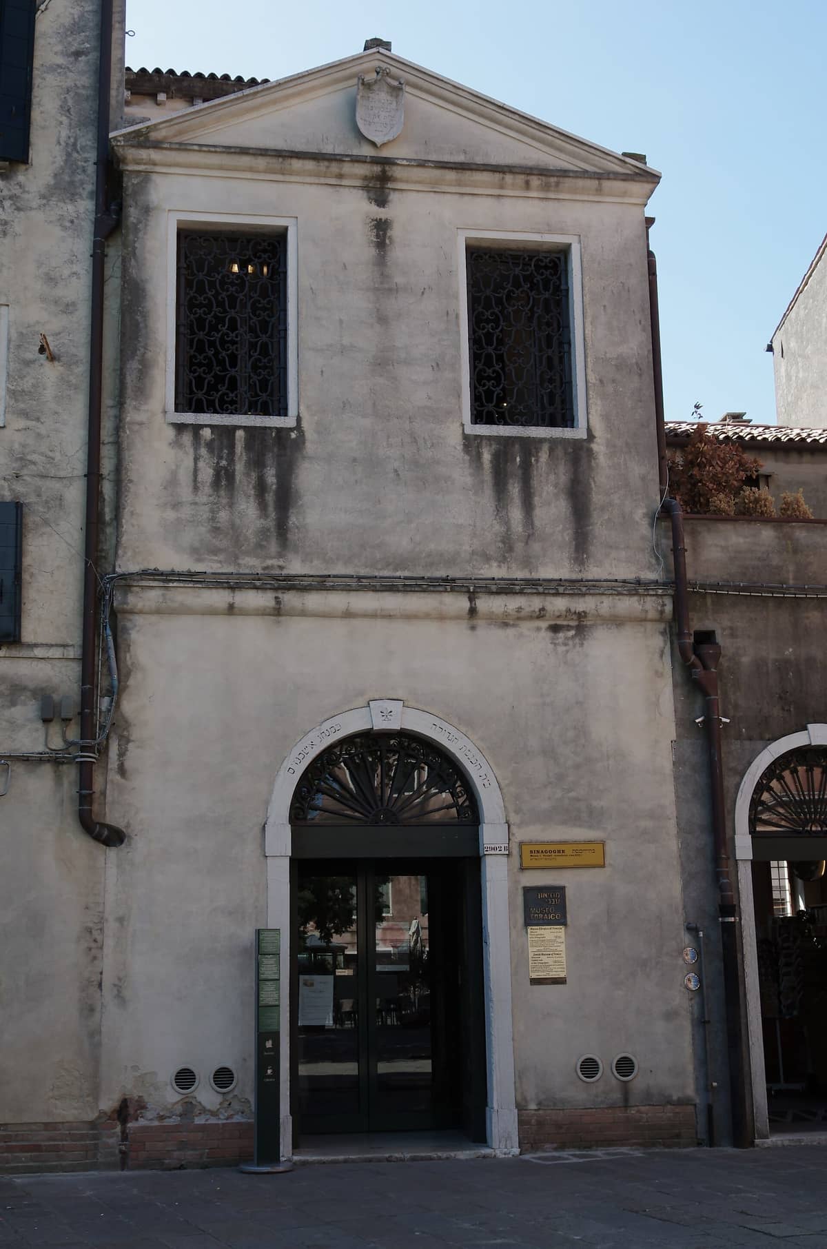 Fassade des Jüdischen Museums Venedig mit verwitterten Steinmauern, gewölbtem Eingang und schmiedeeisernen Fenstergittern im hellen Tageslicht.