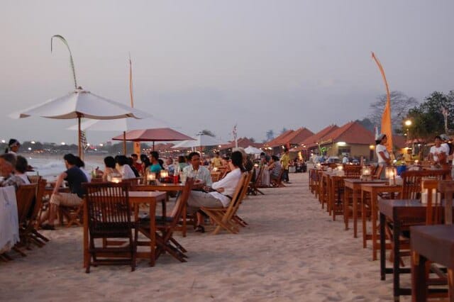 Tavoli per la cena di pesce sulla sabbia della baia di Jimbaran a Bali, con la luce del tramonto sull'oceano