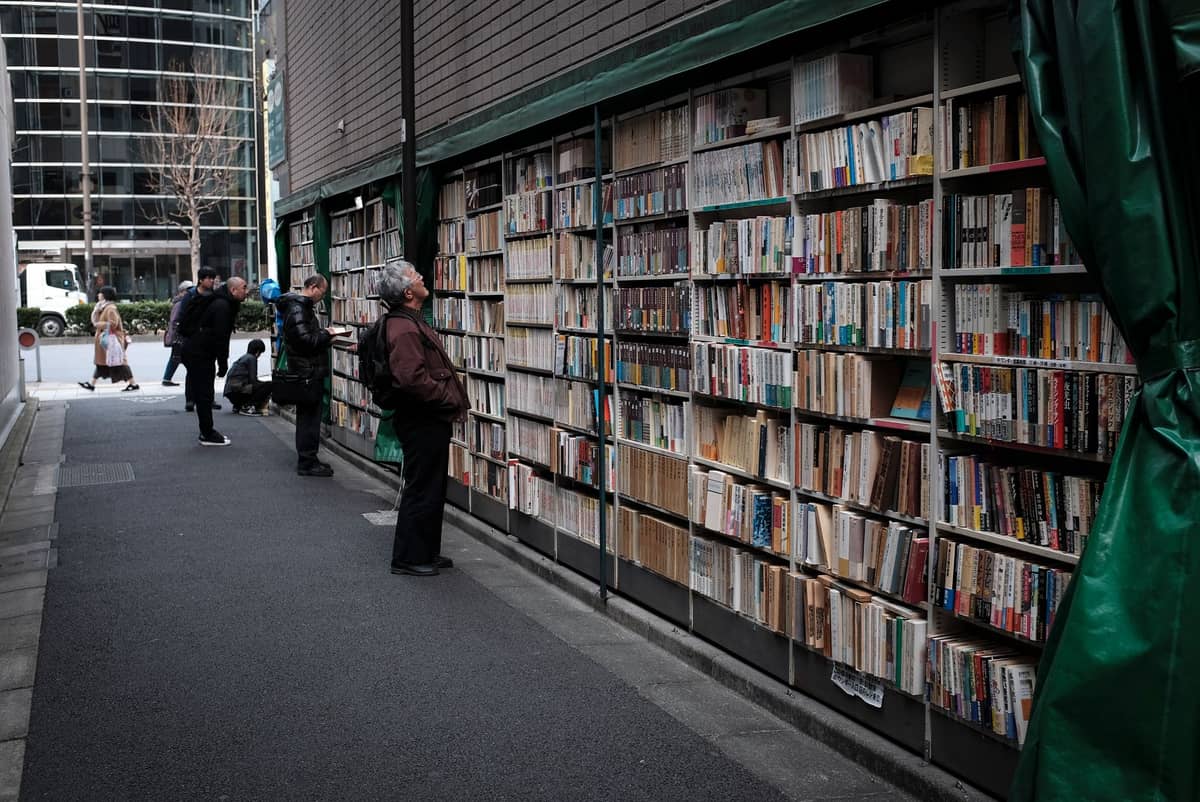 People browsing towering outdoor bookshelves filled with secondhand books along a street in Tokyo’s Jimbocho Book District.
