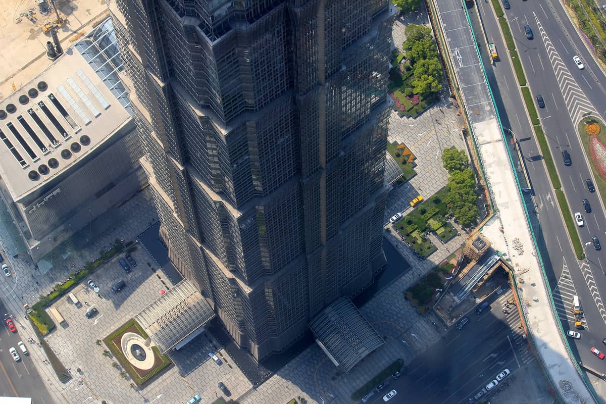 Luftaufnahme senkrecht nach unten auf die pagodenartigen Stufen und die Art-déco-Fassade des Jin Mao Tower, darunter Straßen und Autos.