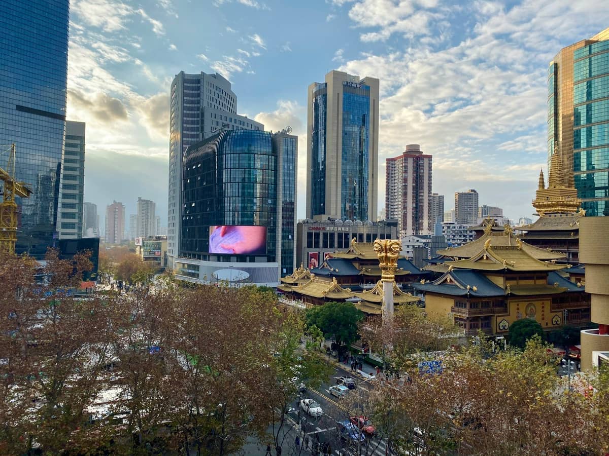 Die goldenen Dächer des Jing'an-Tempels stechen neben modernen Glaswolkenkratzern und baumgesäumten Straßen im Herzen von Shanghais lebhaftem Jing'an-Viertel hervor.