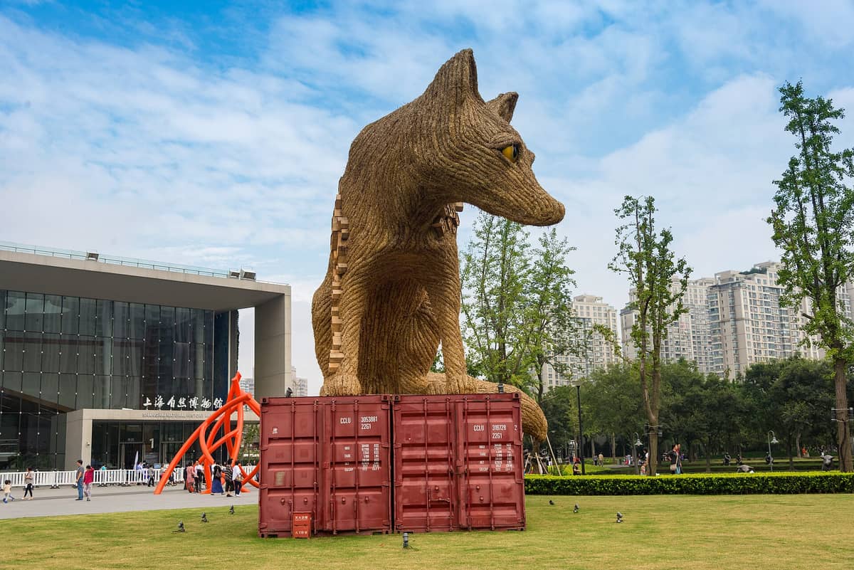 Große Fuchsskulptur aus Naturmaterialien auf roten Schiffscontainern, dahinter das Shanghais Naturkundemuseum und die Skyline im Jing'an Sculpture Park.