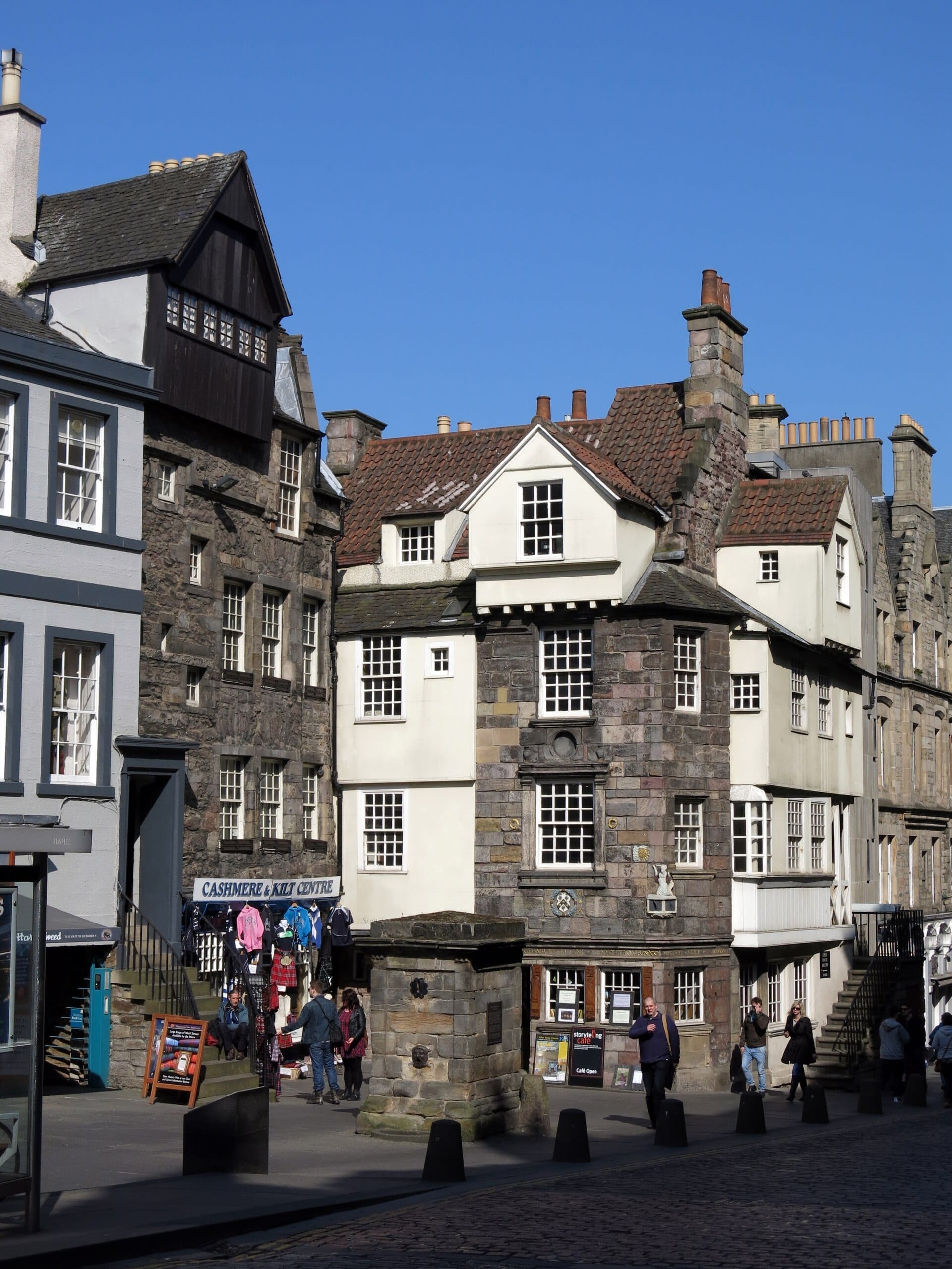Das John Knox House an der Royal Mile in Edinburgh zeigt eine mittelalterliche Steinfassade, weißgerahmte Fenster und Besucher, die unter klarem blauem Himmel spazieren.
