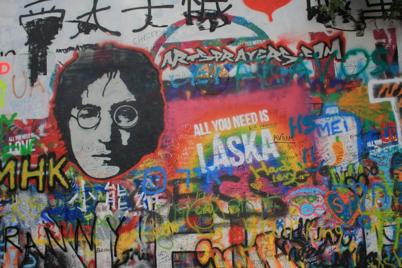 Bunte Graffiti und ein großes Schwarz-Weiß-Porträt von John Lennon an der berühmten John Lennon Wall in Prag, bedeckt mit lebhafter Straßenkunst.