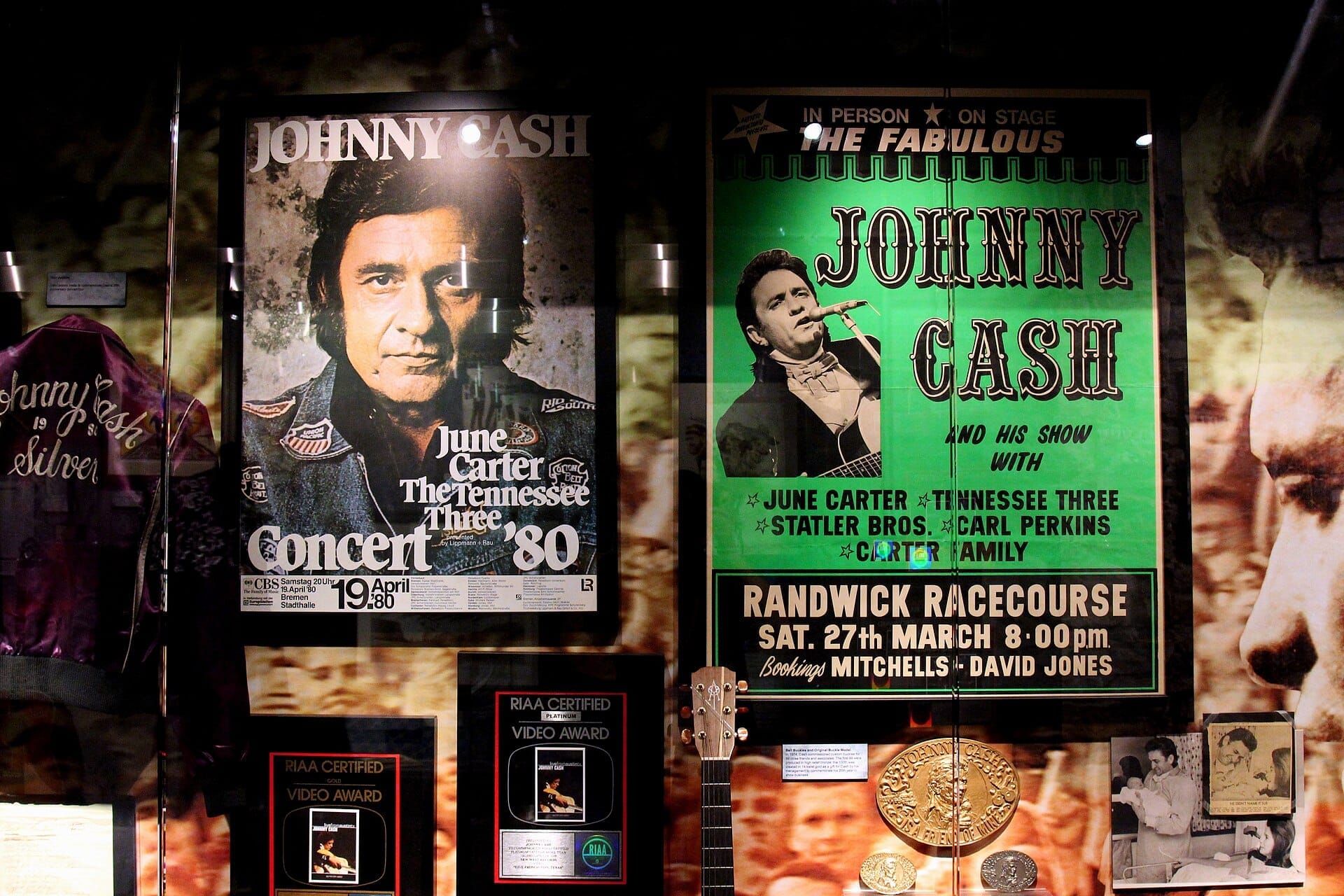 Exhibición del Museo de Johnny Cash con carteles de conciertos vintage, una chaqueta de gira morada y placas de premios RIAA bajo vidrio en una exposición con poca luz.