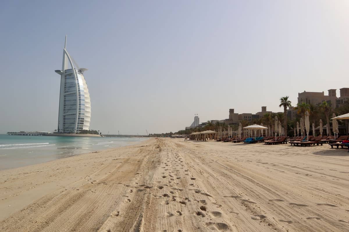 Weiter Blick auf Jumeirah Beach mit dem Burj Al Arab im Hintergrund, ruhigem Meer und sauberem Sandstrand an einem sonnigen Tag.