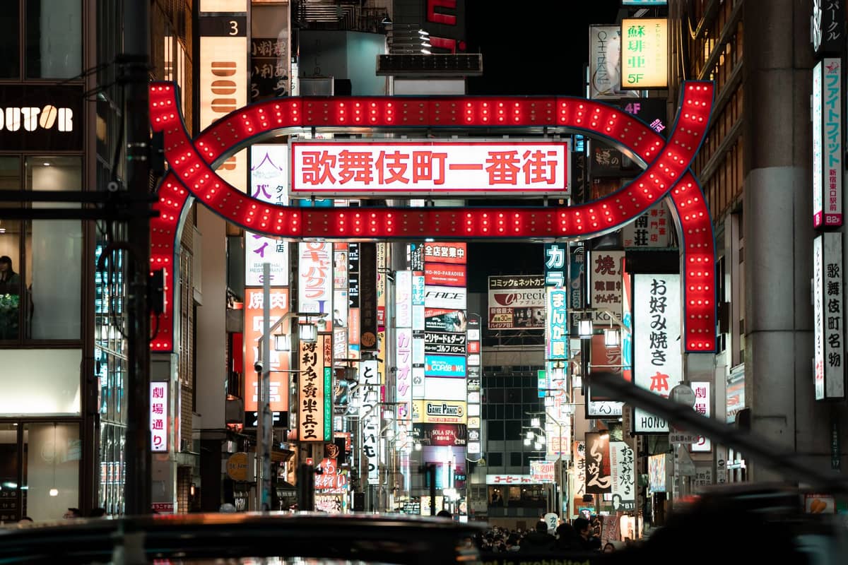 The neon-lit entrance gate to Kabukicho with its distinctive red archway and bright signage, leading into a bustling nightlife district in Shinjuku, Tokyo.
