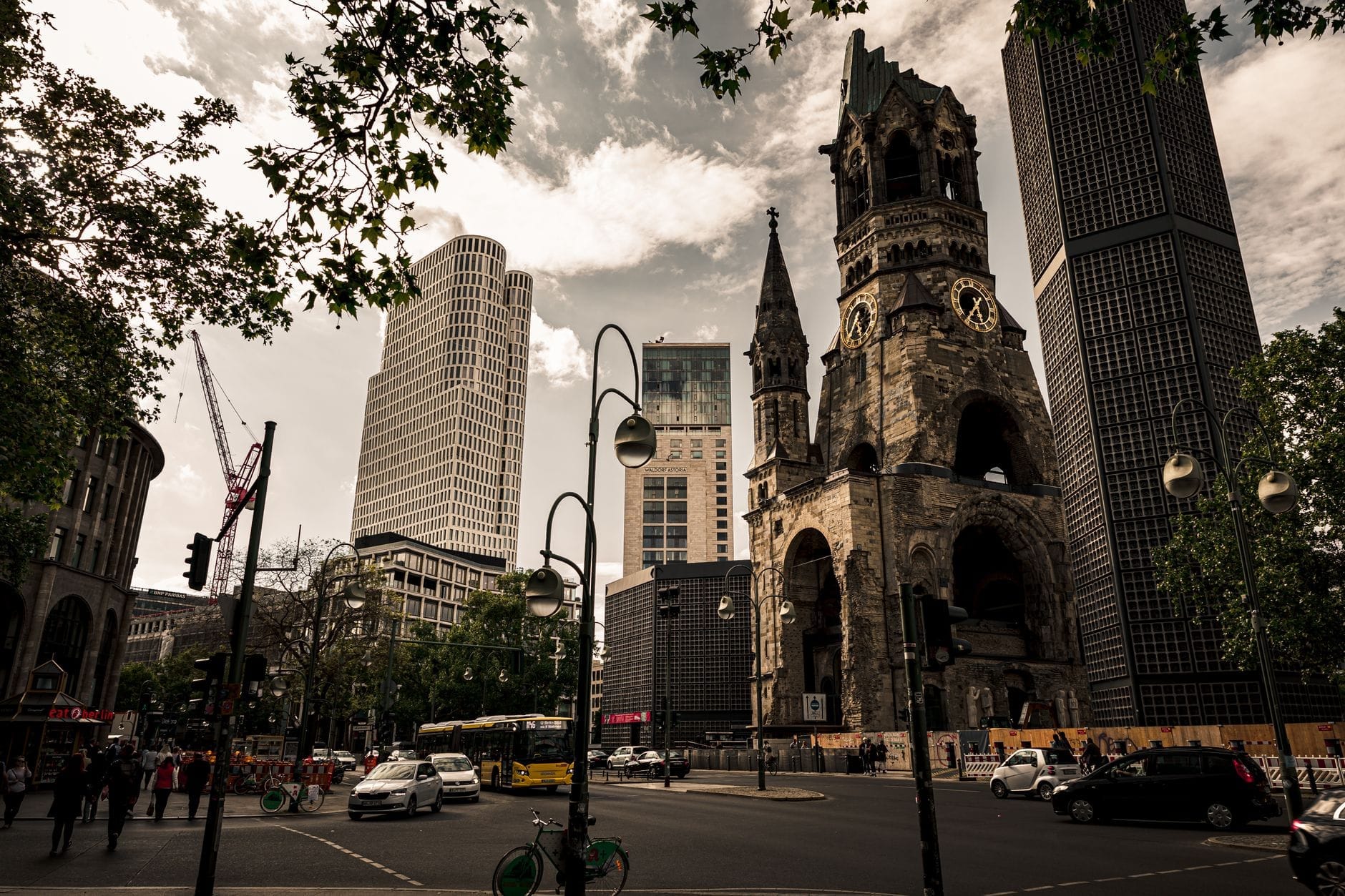 Vista panoramica del campanile in rovina della Kaiser-Wilhelm-Gedächtniskirche, circondato da edifici moderni e dal vivace via vai di Breitscheidplatz a Berlino.