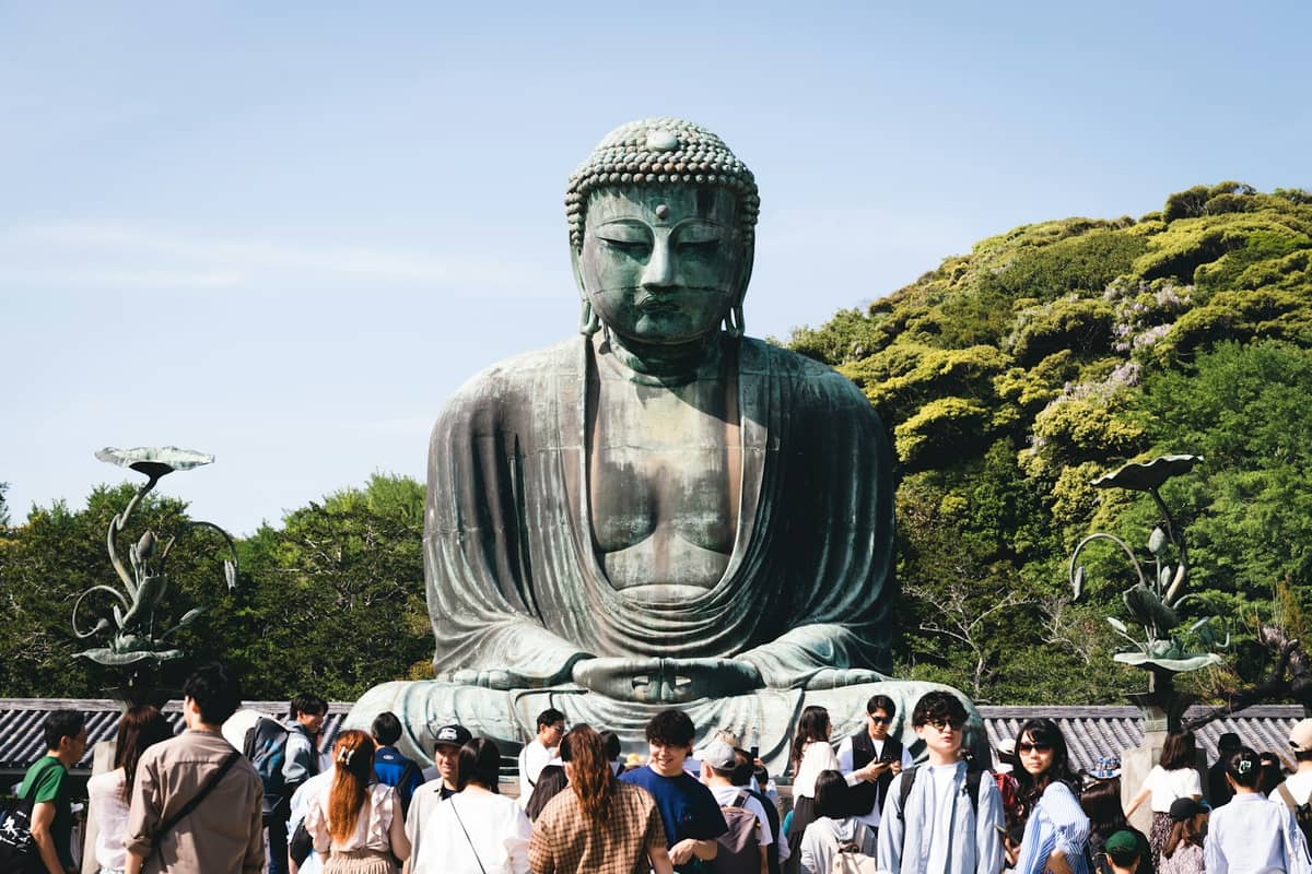 The Great Buddha (Kamakura Daibutsu), an iconic outdoor bronze statue at Kotoku-in temple in Kamakura, with visitors gathered around and lush greenery in the background.
