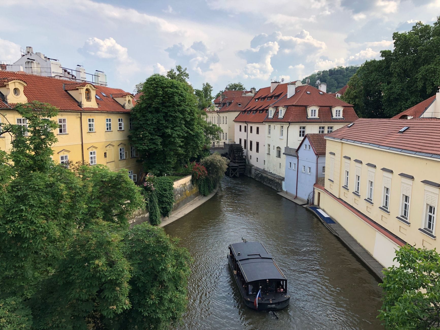 Vista dell'isola Kampa con i suoi colorati edifici barocchi e il tranquillo canale del Čertovka, con una piccola barca che scivola tra gli alberi frondosi nel quartiere storico di Malá Strana a Praga.