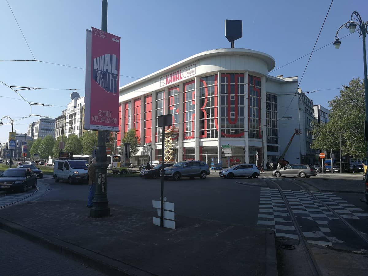 O edifício Kanal – Centre Pompidou em Bruxelas, uma estrutura moderna em branco e vermelho com grandes letras BRUT, visto de uma movimentada intersecção urbana.