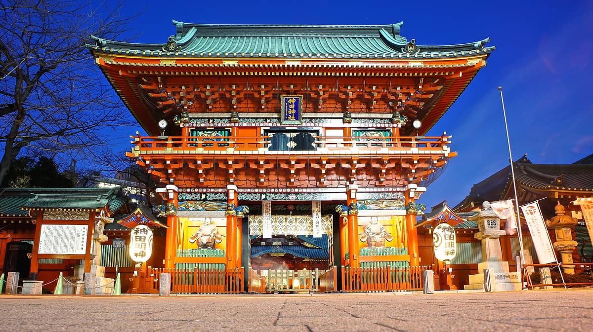Striking evening view of the vividly illuminated main gate (Zuishinmon) of Kanda Myojin Shrine, showcasing elaborate woodwork and traditional Japanese architectural details.