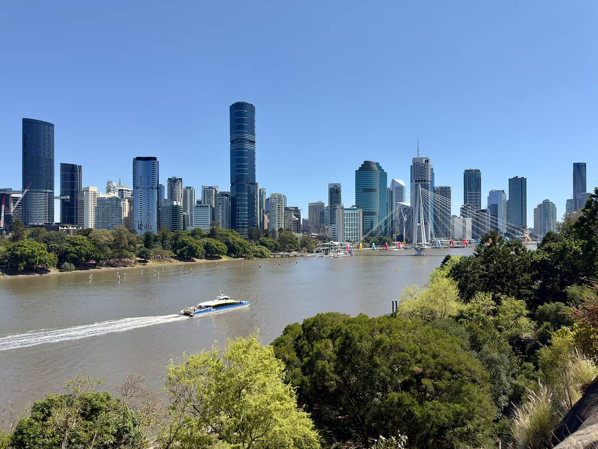 Wide landscape view of the Kangaroo Point Bridge crossing the Brisbane River, with the city skyline in the background under a clear blue sky.