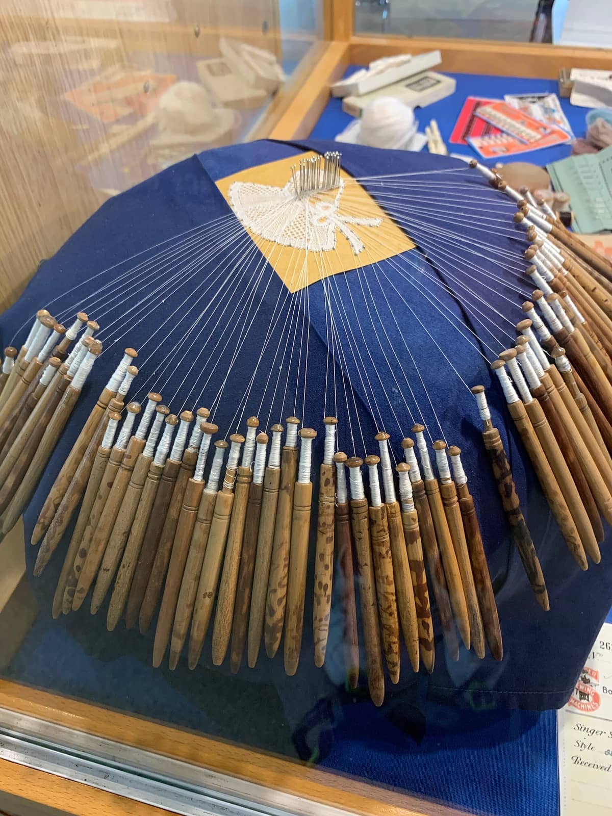 Wooden bobbins and white threads set up on a blue pillow for bobbin lace making, displayed at the Lace Centre in Bruges.