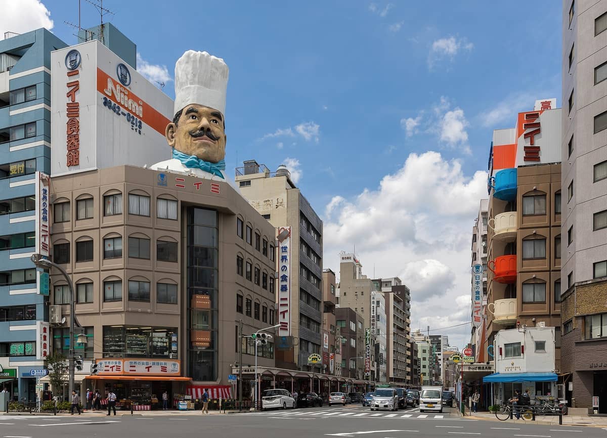 Street view of Kappabashi Kitchen Town in Tokyo, featuring the iconic Niimi chef statue atop a multi-story building on a clear day.