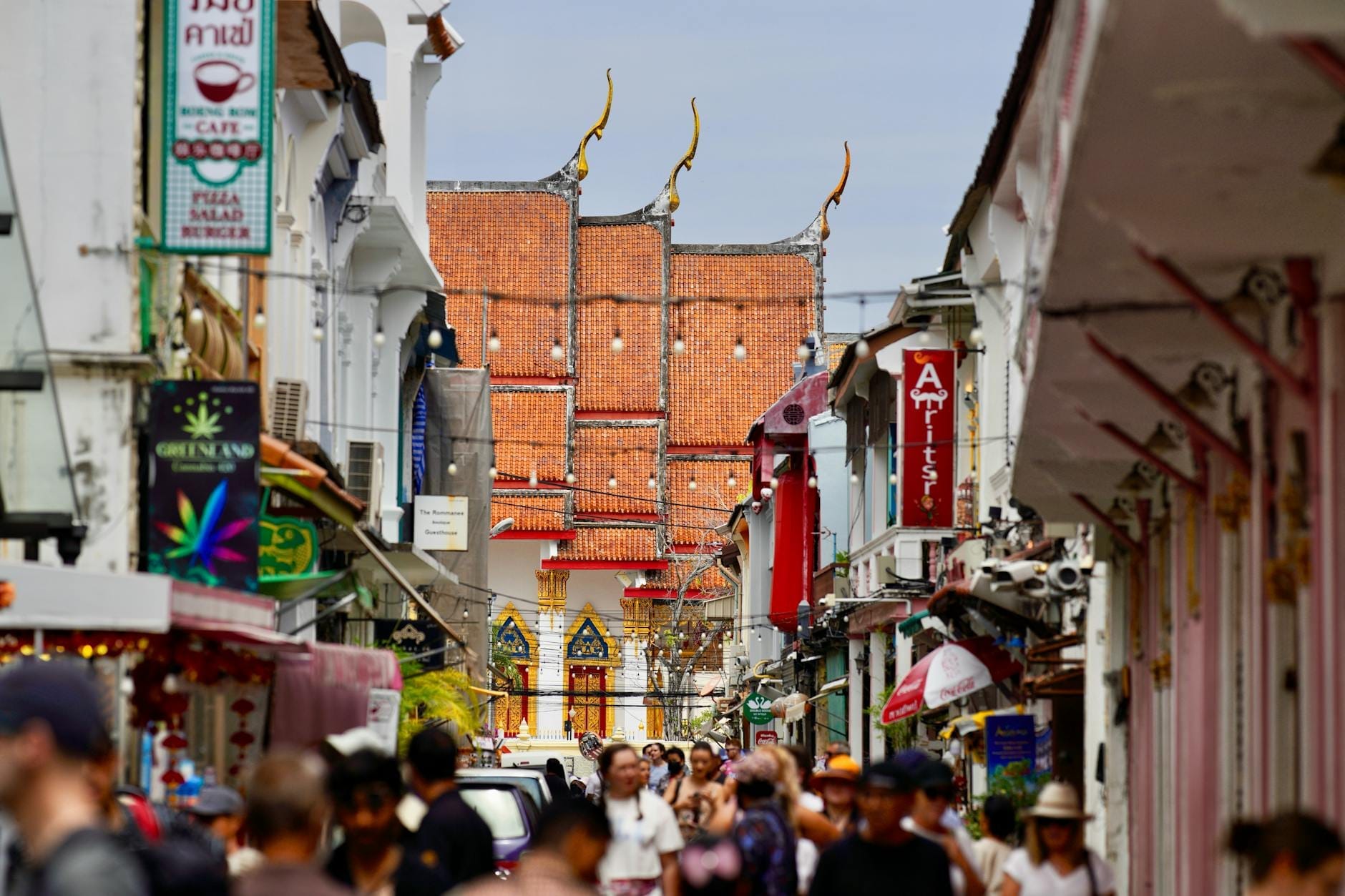 Busy street scene leading up to Karon Temple Market, with colorful signs, historic buildings, and an ornate temple roof in the background.