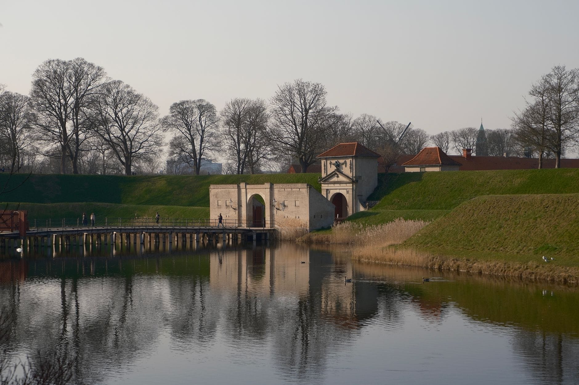 Vista del cancello d'ingresso del Kastellet, del fossato e dei bastioni verdi alberati, riflessi nell'acqua immobile in una giornata serena a Copenaghen.