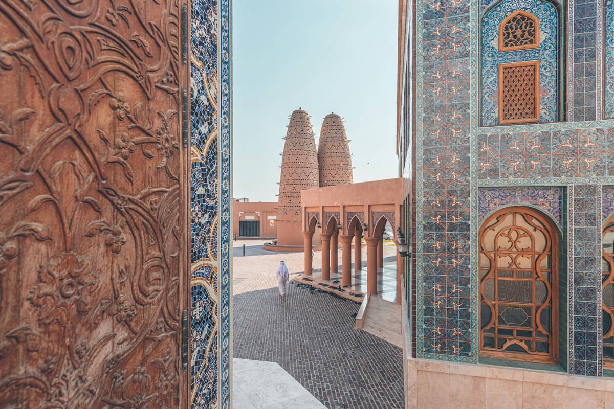 Aufwendig blau gekacheltes Gebäude und traditionelle katarische Architektur im Katara Cultural Village mit Taubentürmen im Hintergrund an einem klaren Tag.