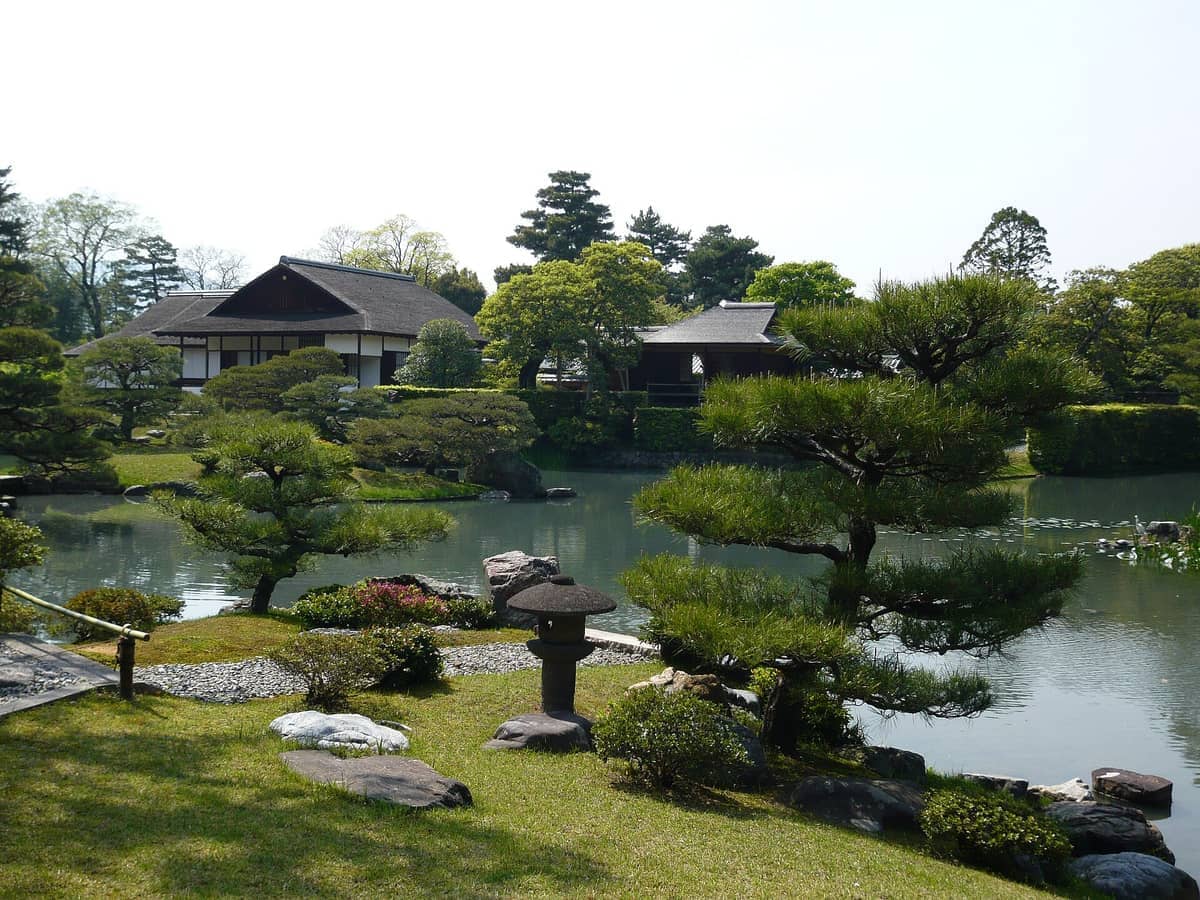 Traditional wooden buildings and a pond surrounded by manicured trees and stone lanterns at Katsura Imperial Villa in Kyoto, Japan.