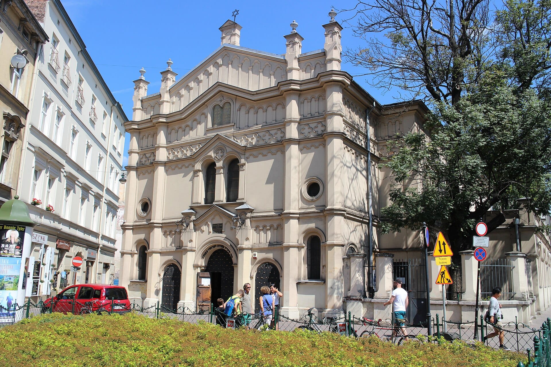 อาคารภายนอกของ Tempel Synagogue อันหรูหราในคาซีเมียร์ซ คราคูฟ มีคนเดินผ่านและอาคารเมืองอยู่ท่ามกลางท้องฟ้าสีฟ้าใส