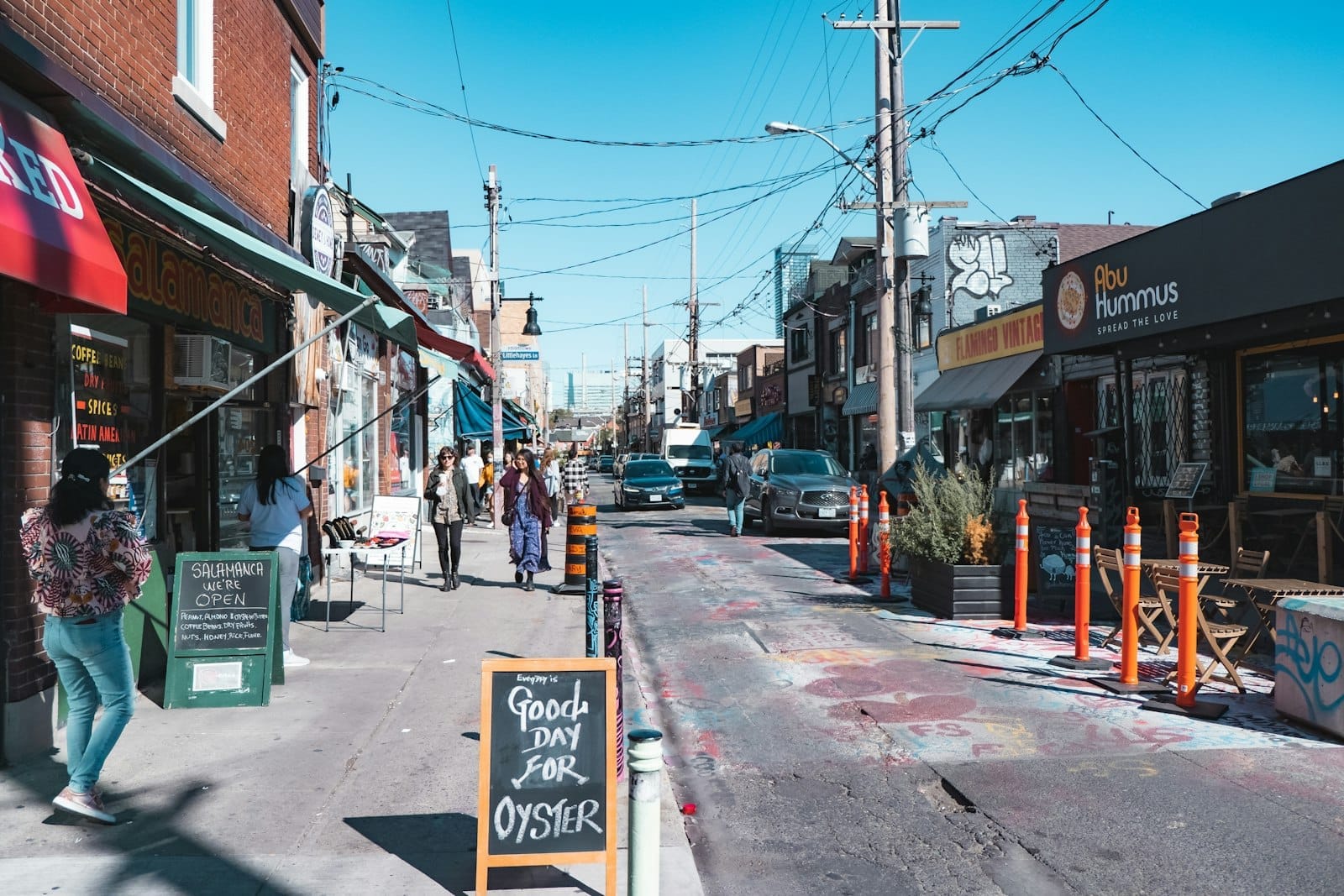 ชีวิตชีวาบนถนน Kensington Market ร้านค้าสีสันสดใส ป้ายคาเฟ่ คนเดินพลุกพล่าน และหน้าร้านไม่ซ้ำใคร ท่ามกลางแดดอบอุ่นในโตรอนโต