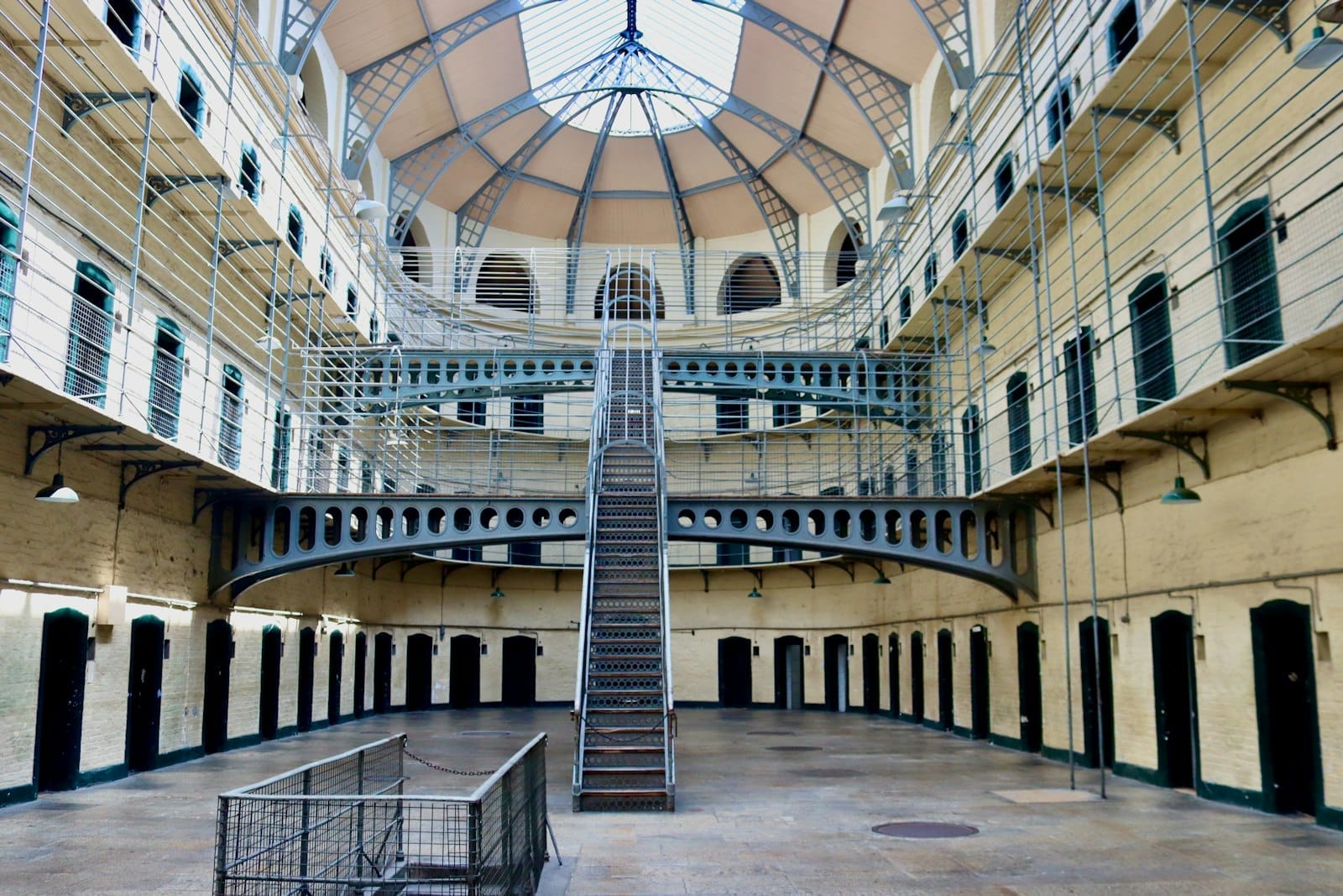 บรรยากาศภายใน Kilmainham Gaol ที่สว่าง โถงกว้าง บันไดกลาง เดินโล่งด้วยทางเดินโลหะและเพดานโค้งใต้แสงธรรมชาติ