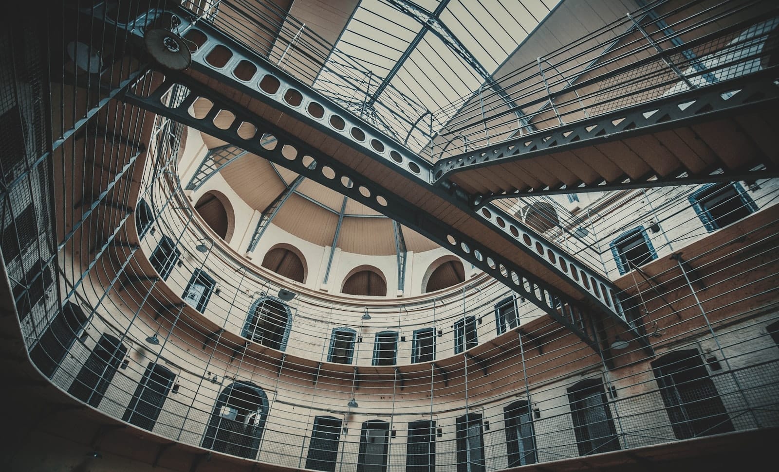 Vista interna del Kilmainham Gaol Museum, con passerelle in ferro vittoriano, multiple porte di celle e un soffitto a cupola illuminato da un lucernario.