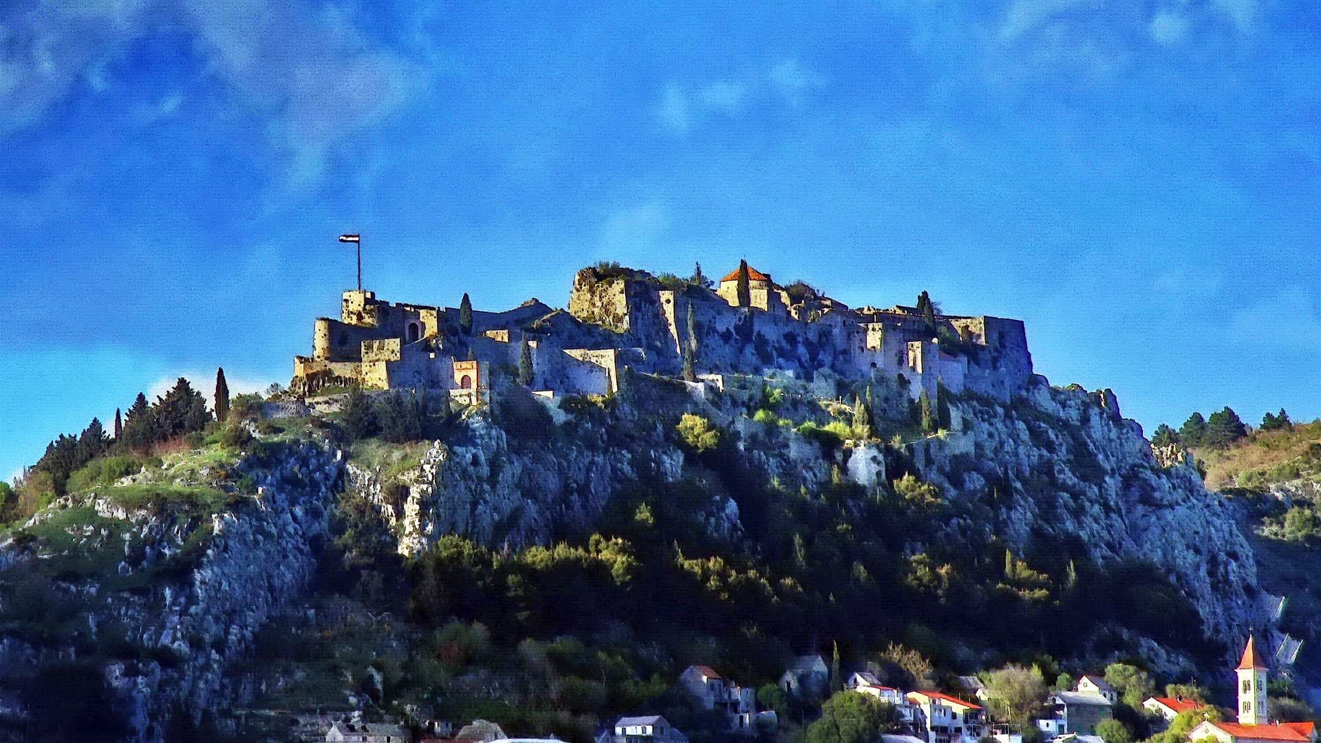 ป้อมปราการ Klis ตั้งอยู่บนยอดเขาหินเหนือเมือง Split พร้อมกำแพงหินและหอคอยที่สว่างไสวตัดกับท้องฟ้าสีฟ้าสดใส