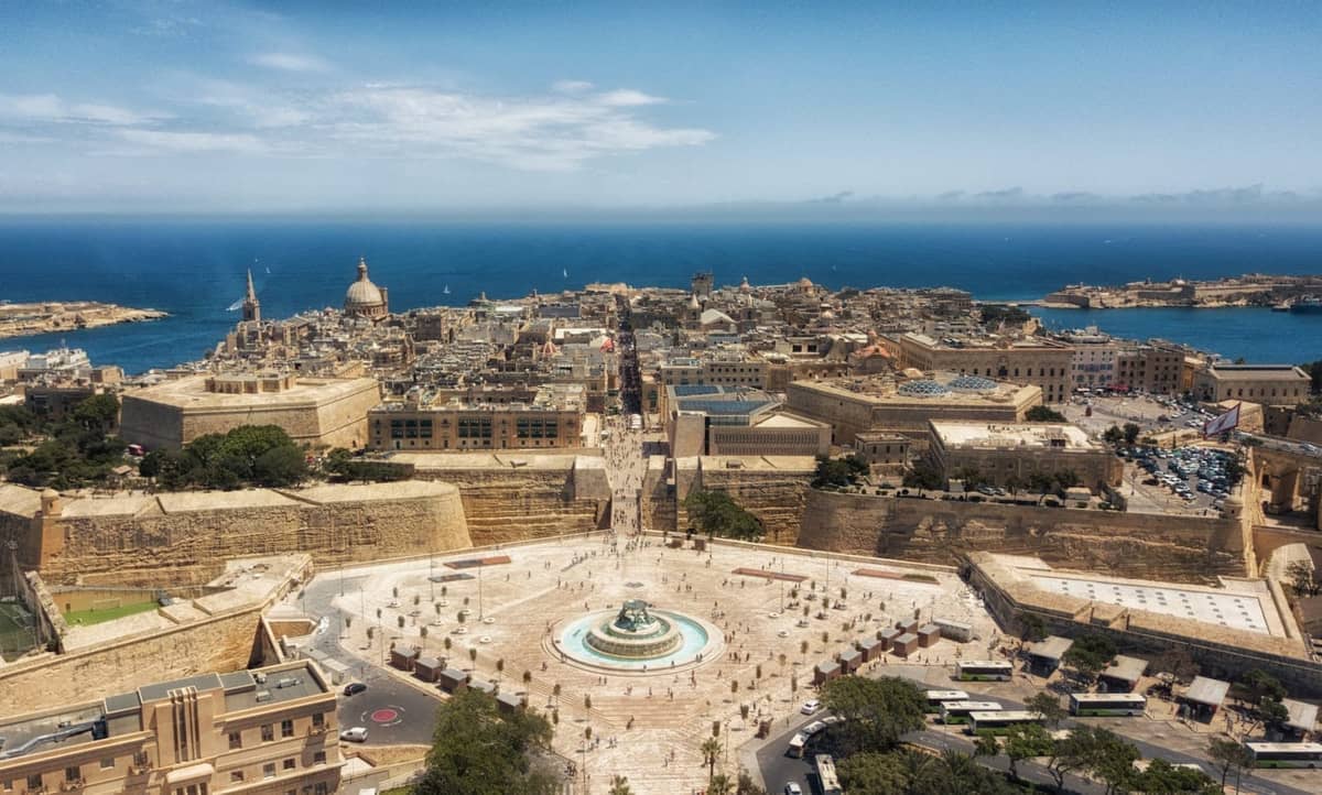 Vista aérea de La Valeta con sus murallas defensivas, la plaza central de la ciudad y el puerto circundante bajo un cielo azul.