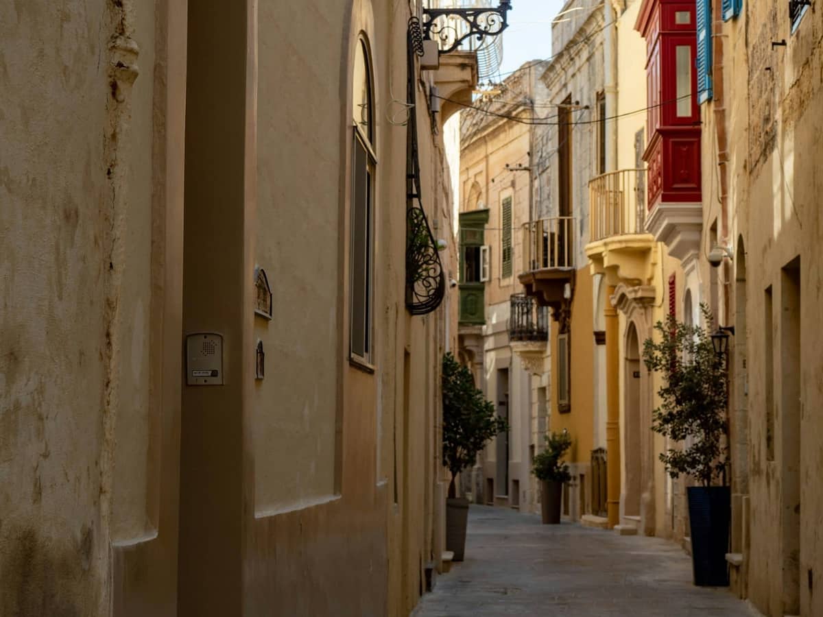 Calle estrecha de piedra en Birgu, Malta, flanqueada por coloridos balcones y plantas en macetas. El encantador ambiente histórico encaja perfectamente con el entorno de las Tres Ciudades.