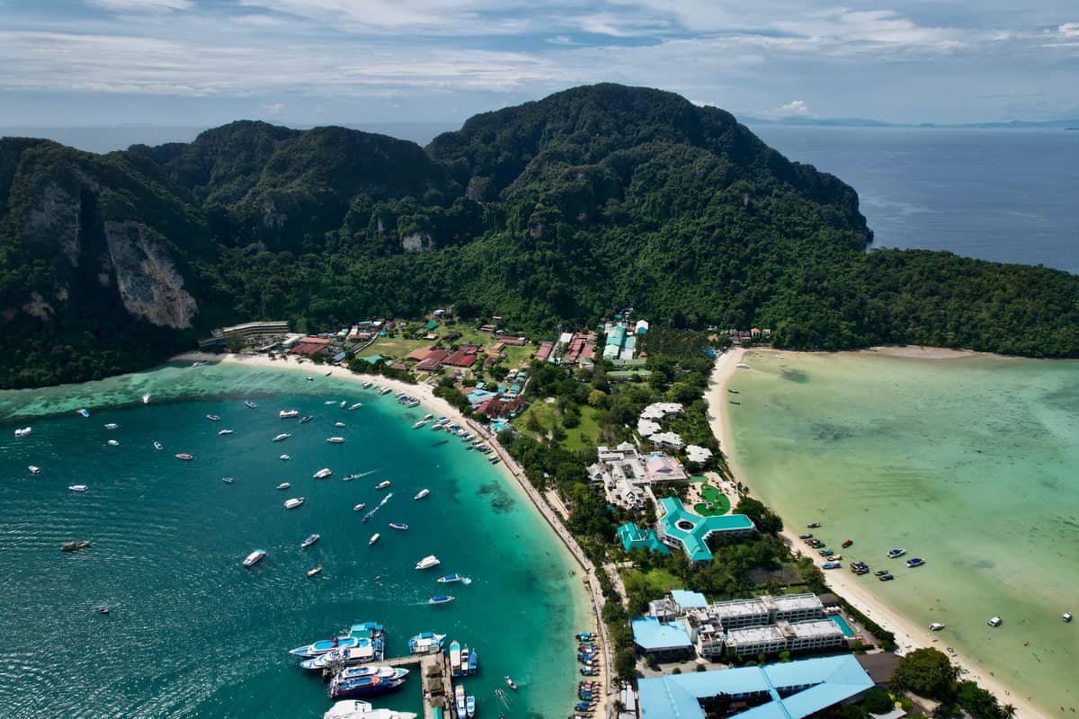 Vista aérea de Koh Phi Phi Don con el pueblo central, colinas boscosas, bahías turquesas, playas y barcos anclados a lo largo de la costa.