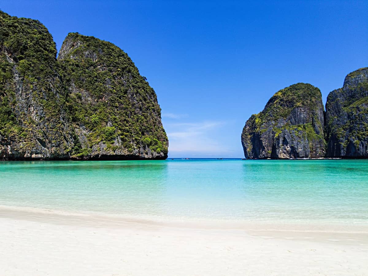 Makellos weißer Sandstrand und kristallklares türkisfarbenes Wasser der Maya Bay, eingerahmt von dramatischen Kalksteinklippen auf Koh Phi Phi Leh unter strahlend blauem Himmel.
