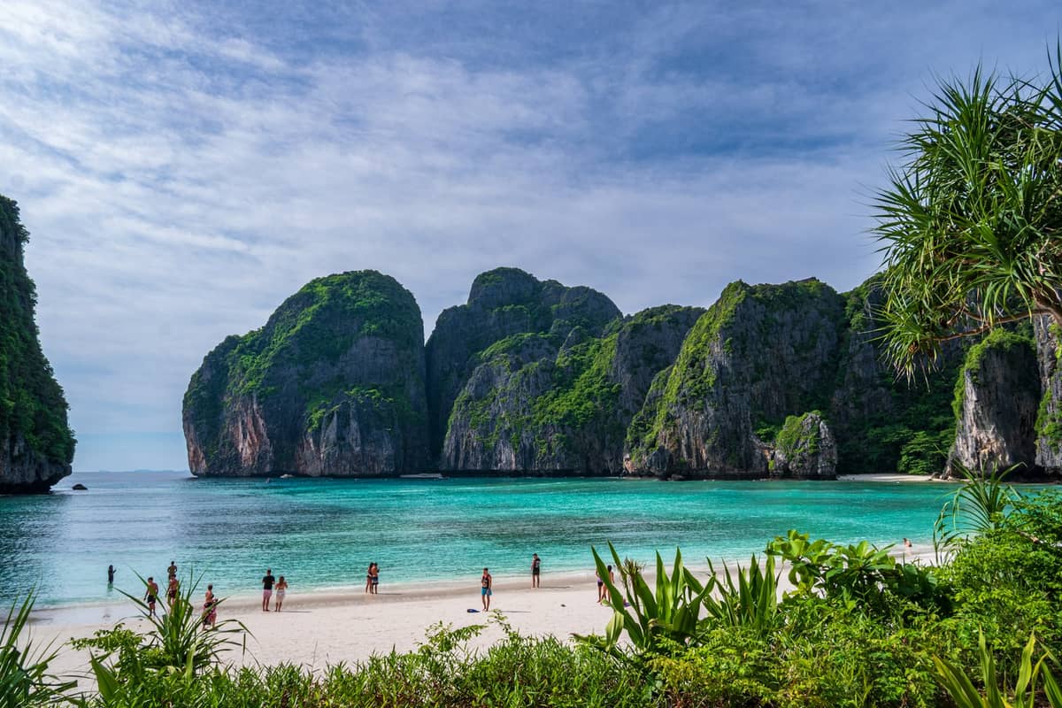หน้าผาหินปูนเขียวชอุ่มกับน้ำทะเลสีมรกตที่อ่าวมาหยา เกาะพีพี ชายหาดทรายขาว มีนักท่องเที่ยวเพลินกับวิว