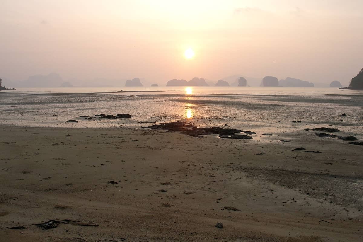 Amanecer o atardecer sobre la tranquila playa de Koh Yao Noi, con arena en primer plano, llanuras mareales y los karsts de piedra caliza de la Bahía de Phang Nga al fondo.