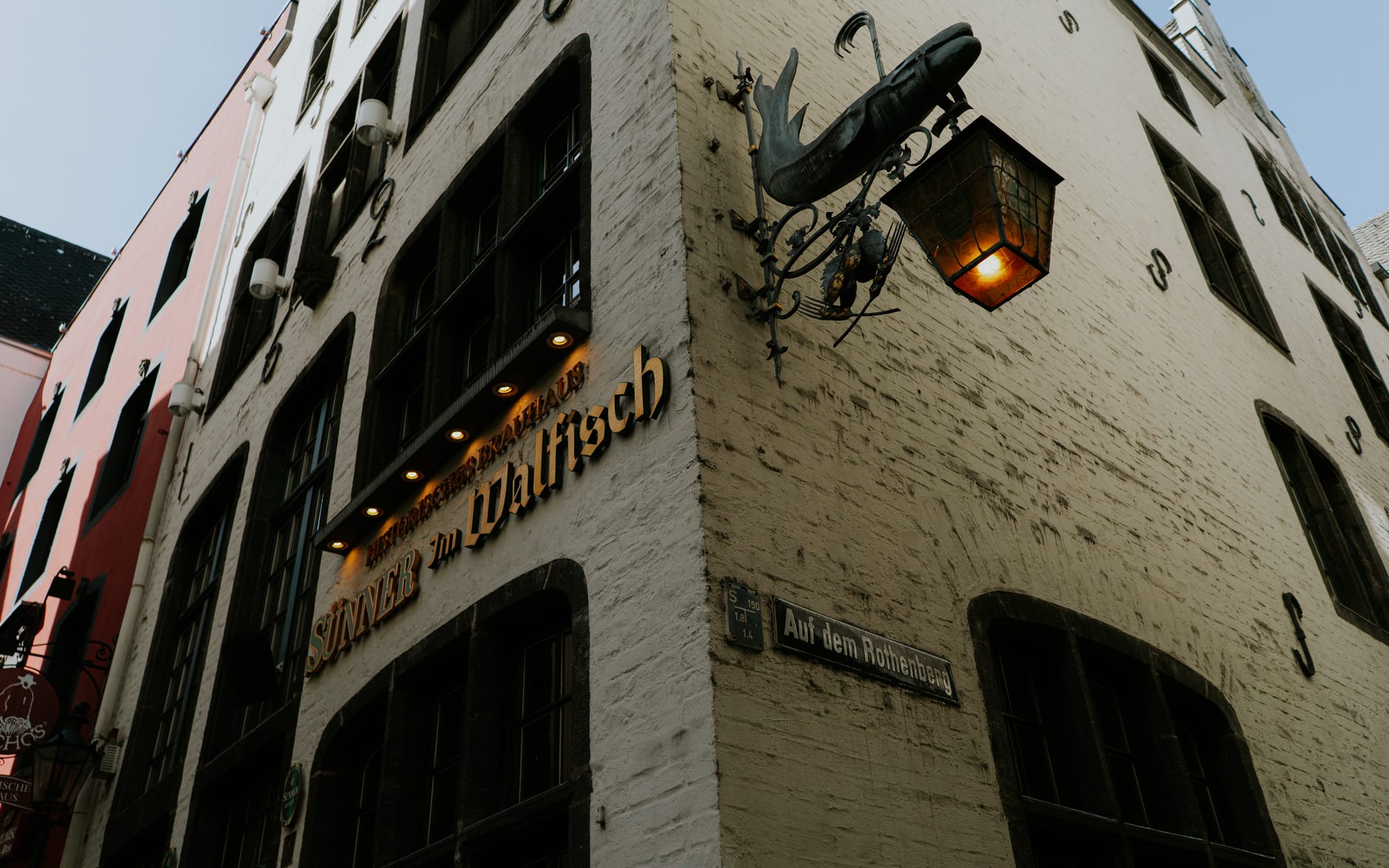 มุมอาคาร Brauhaus เคิลช์แบบดั้งเดิมในโคโลญจน์ มีป้ายร้านและโคมแขวนเหนือตัวป้ายถนน