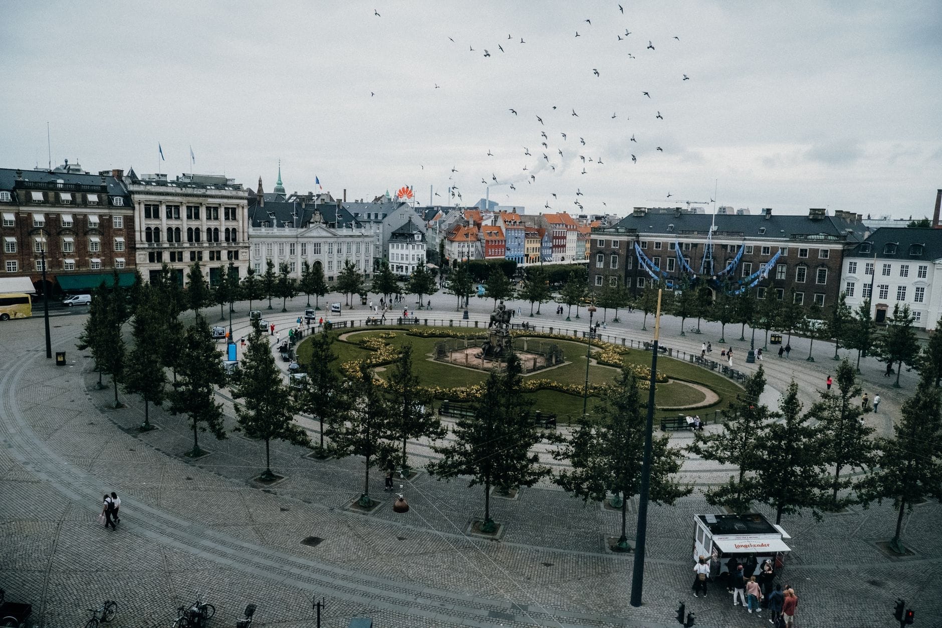 Vista ampia di Kongens Nytorv a Copenaghen, con la statua centrale e il giardino, circondati da edifici storici e persone che passeggiano.