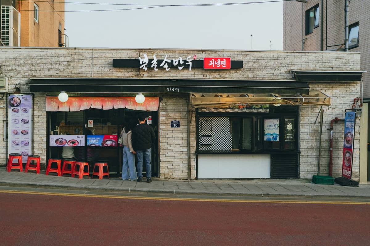 Vista da rua de um restaurante de churrasco coreano em Seul com letreiros em coreano, menus expostos e banquinhos do lado de fora em uma noite tranquila.