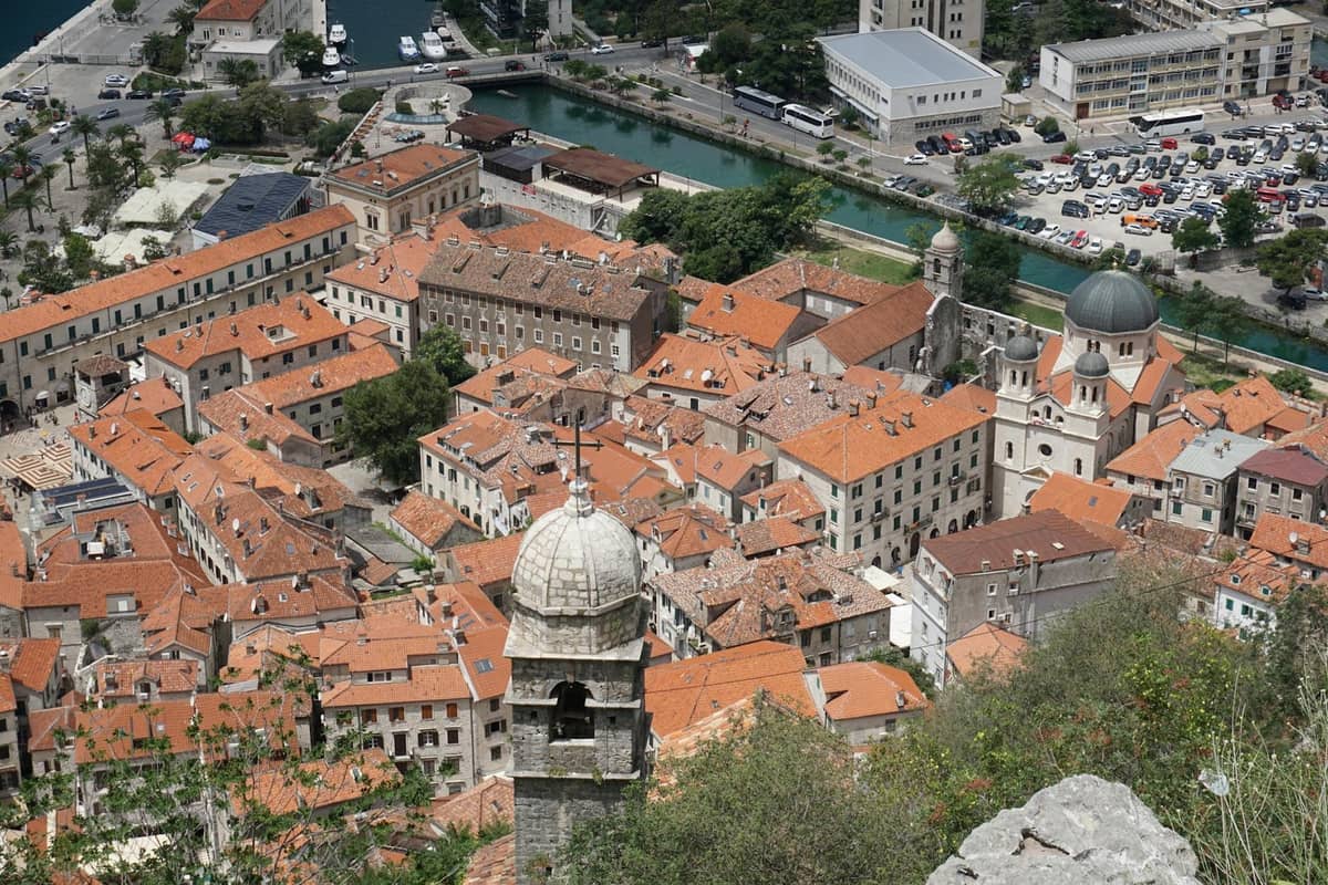Aerial view of Kotor's old town with orange-tiled roofs, historic buildings, churches, and medieval fortifications.