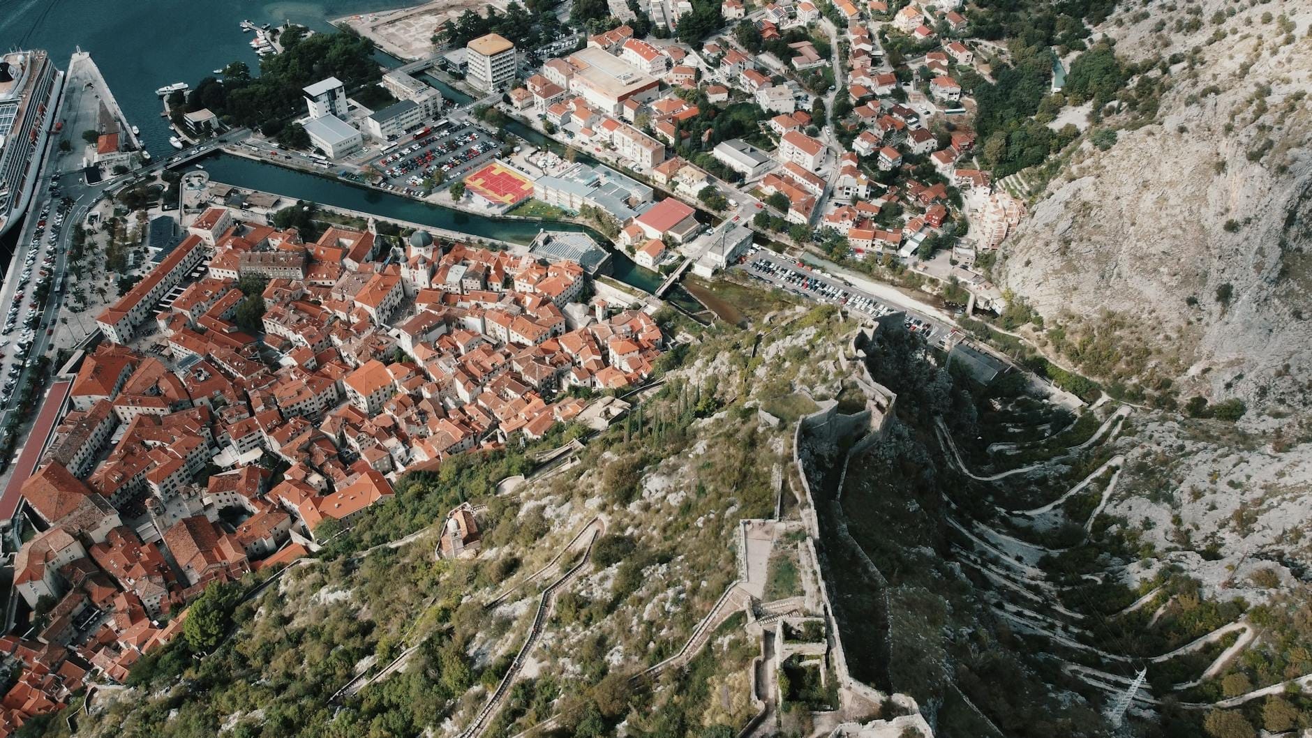 Una spettacolare vista aerea della città vecchia di Kotor con le mura che zigzagano lungo i ripidi pendii del Monte San Giovanni, mostrando le fortificazioni che si ergono sopra la baia adriatica.