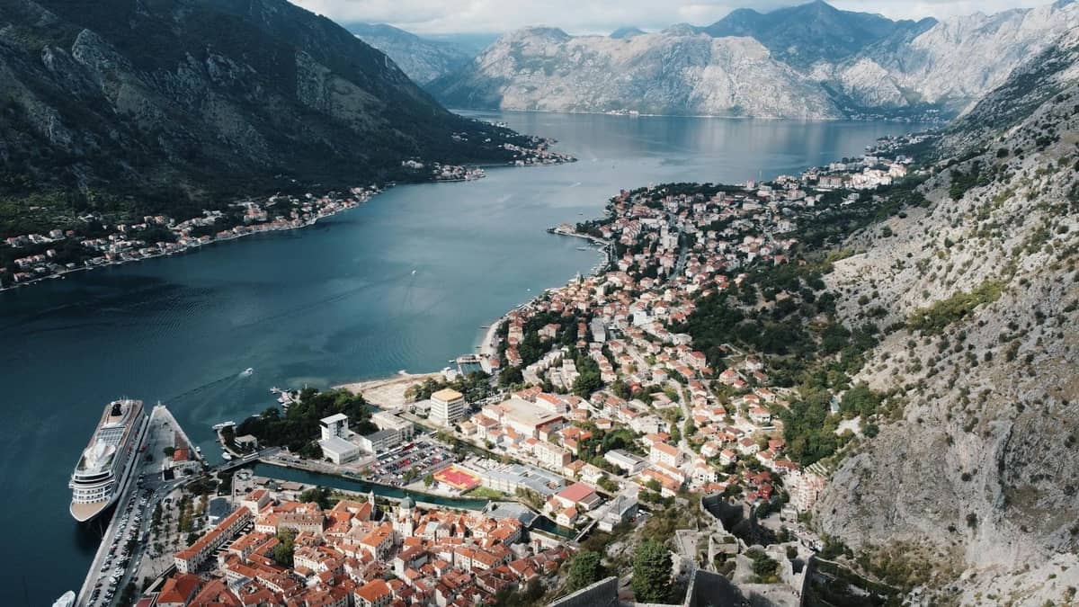 Aerial view of Kotor’s old town, city walls, cruise port, and dramatic bay surrounded by steep mountains, showing the city layout.