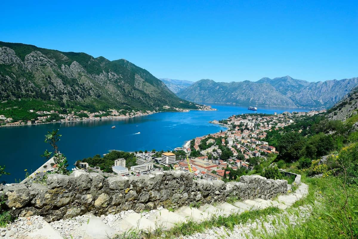 Panoramic view from Kotor Fortress overlooking the Bay of Kotor, town, and surrounding mountains on a clear sunny day.