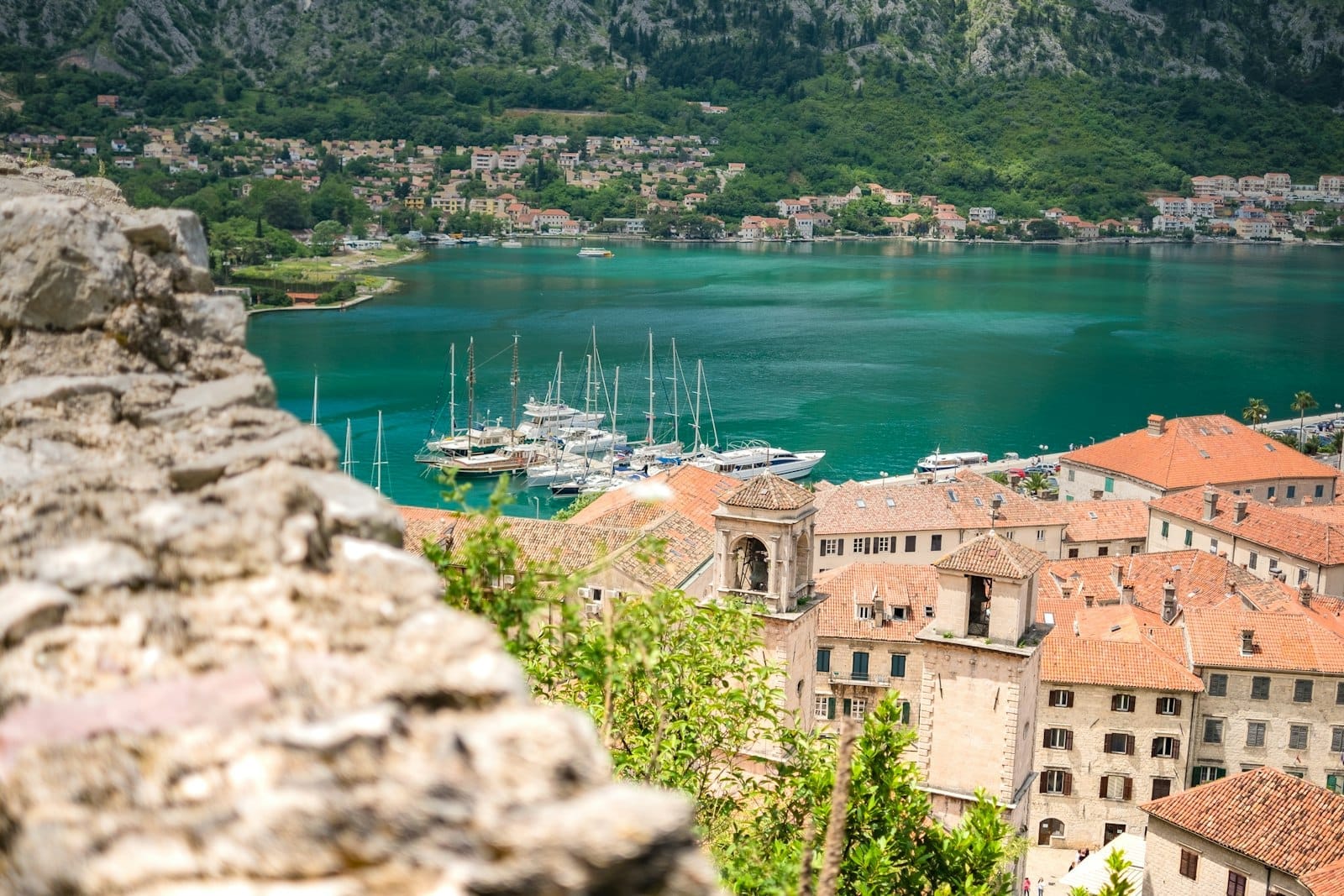 Vista da cidade antiga de Kotor com telhados de telhas vermelhas, edifícios de pedra e uma marina repleta de iates diante da turquesa Baía de Kotor.