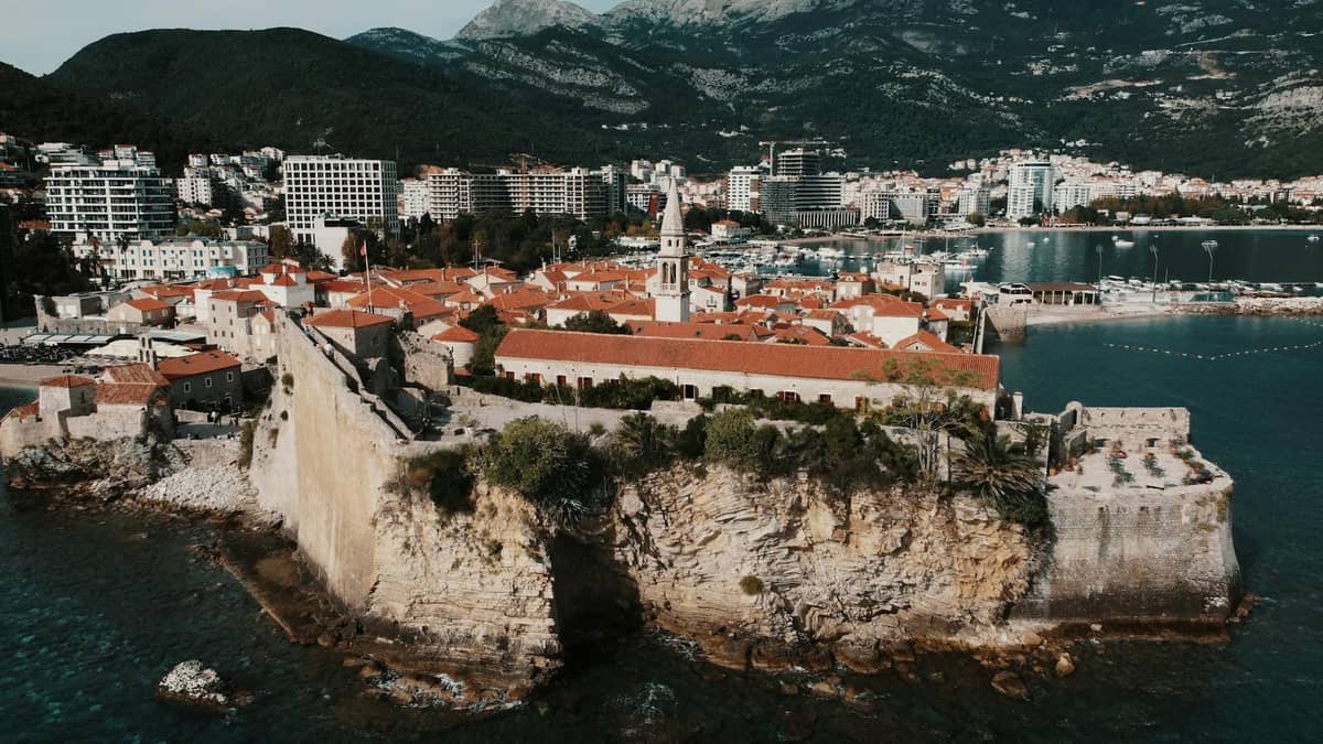 Aerial view of Budva's old town and coastal fortifications with Kotor Bay mountains in the background, illustrating neighboring viewpoints near Kotor.