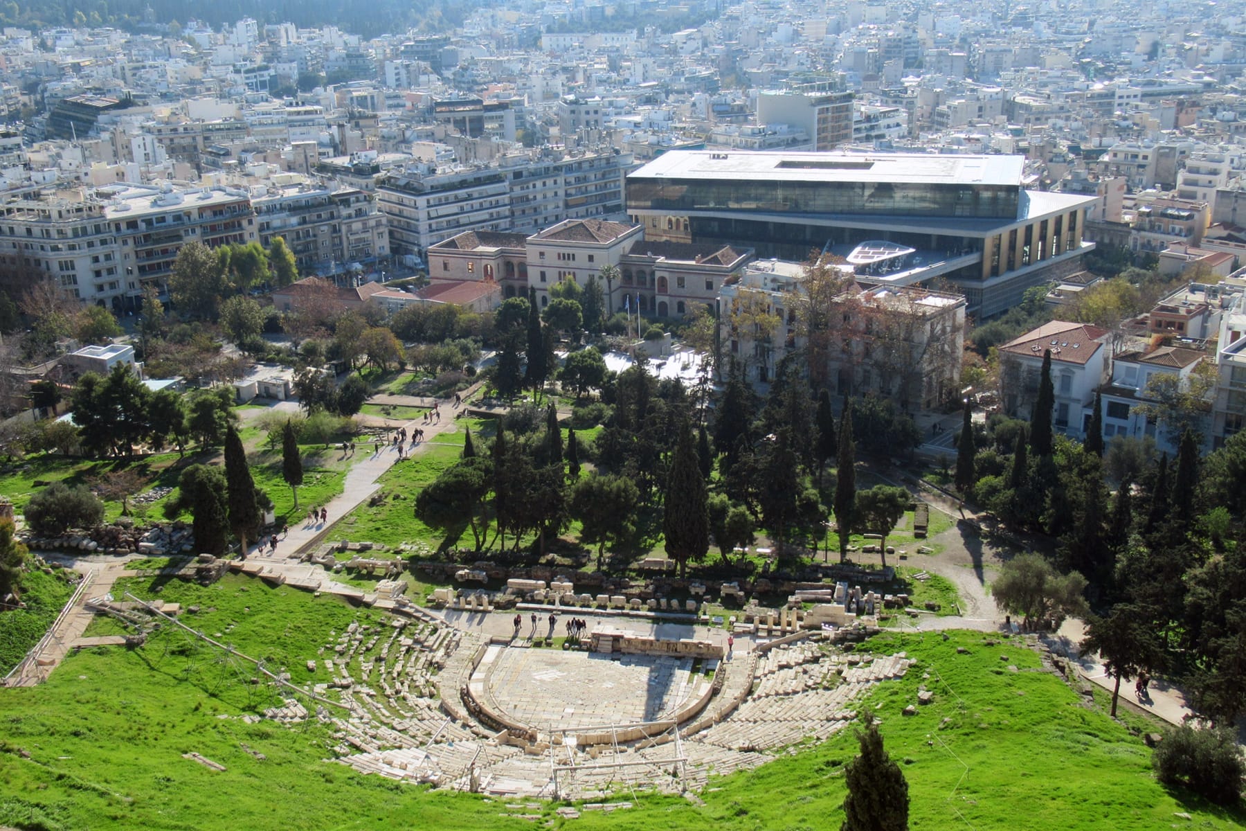 วิวของ Theatre of Dionysus โบราณใน Koukaki พร้อมอาคารสมัยใหม่และ Acropolis Museum เป็นฉากหลังภายใต้แสงกลางวันที่แจ่มใส