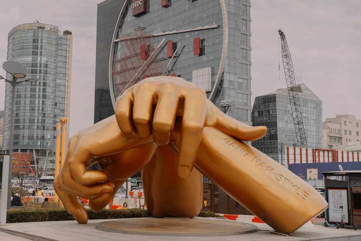 Grande escultura dourada de uma mão fazendo o gesto de coração com os dedos, localizada em frente a edifícios modernos no Starfield COEX Mall em Gangnam, Seul, uma atração popular do K-pop.
