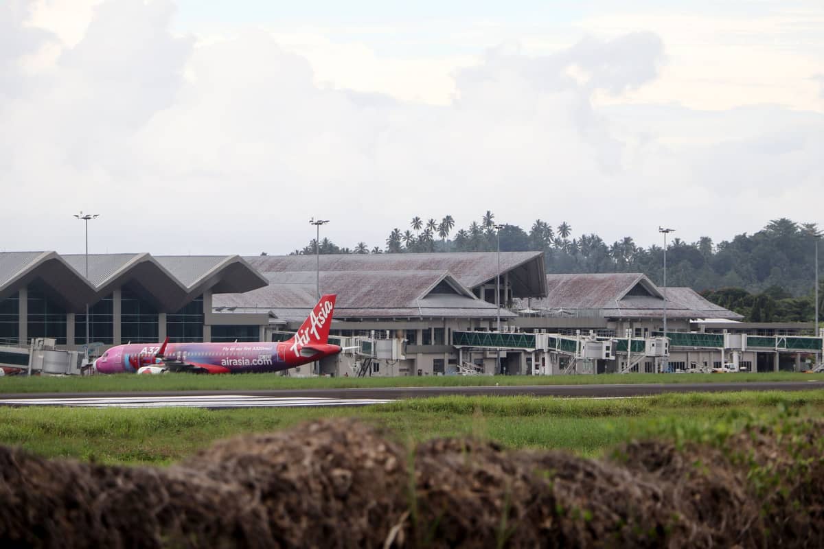 Außenansicht des Terminals des Krabi International Airport mit einem AirAsia-Flugzeug auf der Startbahn, umgeben von Grünflächen und tropischen Bäumen.